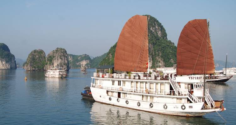 Barco junco tradicional blanco con velas marrones se desliza por las aguas esmeralda de la Bahía de Halong.
