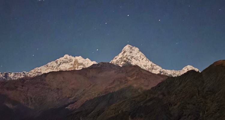 Vue nocturne des pics himalayens étoilés faiblement illuminés au-dessus des vallées sombres.