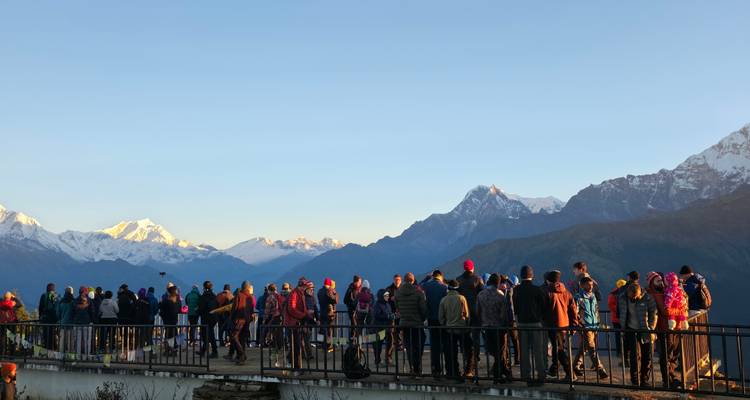 Les foules vêtues de vestes colorées admirent le lever de soleil sur un vaste panorama himalayen depuis Poon Hill.