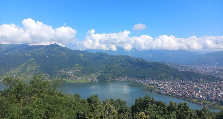 Vue panoramique sur le lac Phewa, les collines en terrasses et la ville de Pokhara sous des nuages blancs tourbillonnants.