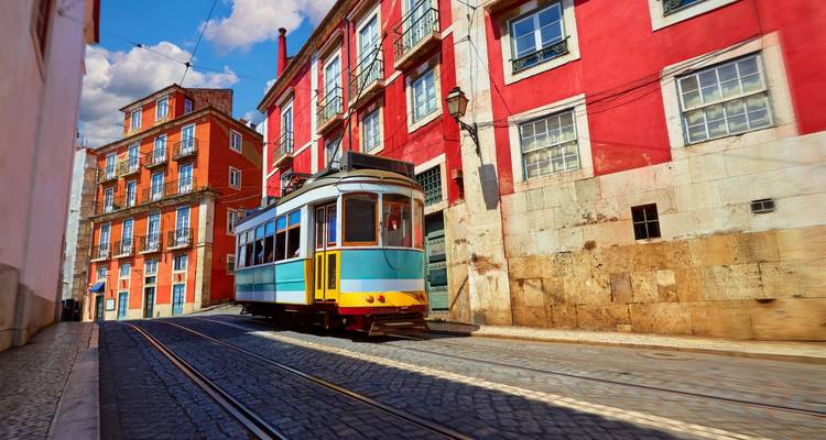 Le célèbre tramway jaune et bleu de Lisbonne montant une rue pavée bordée de vieux immeubles colorés sous un ciel bleu.