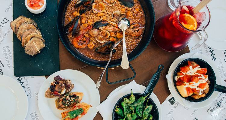 Vue de dessus d'un assortiment de tapas ibériques et de paella aux fruits de mer avec du sangria sur une table en bois dressée pour le partage.