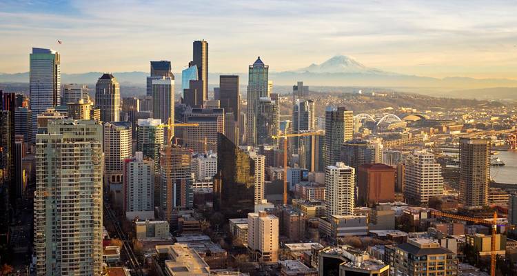 Panoramic view of a modern skyline with Mount Rainier in the hazy background during golden hour.