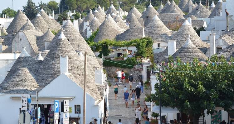 Straße mit traditionellen Trulli-Häusern und Touristen.