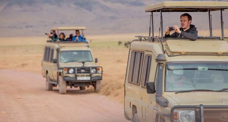 Véhicules de safari avec des touristes dans un paysage de savane.