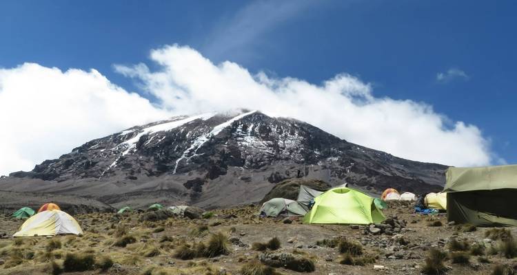Tentenkamp aan de voet van een besneeuwde bergtop met blauwe lucht.