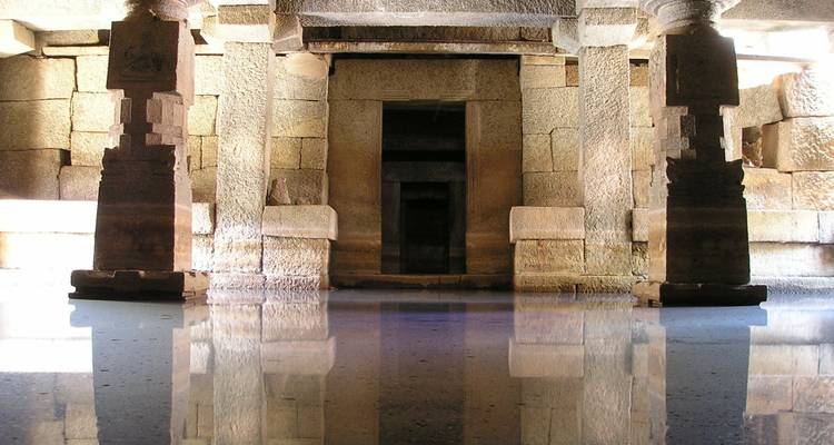 Antiguo salón de piedra con pilares reflejados en agua quieta creando una atmósfera misteriosa