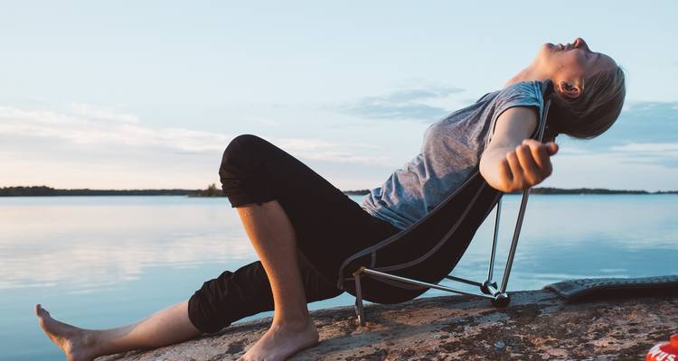 Personne se détendant sur un rivage rocheux au bord de l'eau pendant le coucher du soleil.