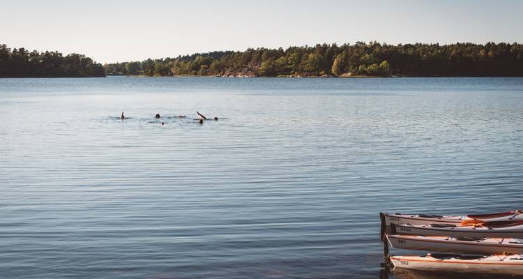 Des gens qui nagent dans un lac avec des kayaks le long du rivage.