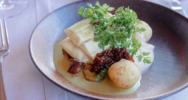 Un plat gastronomique avec du poisson, des pommes de terre et une sauce verte.