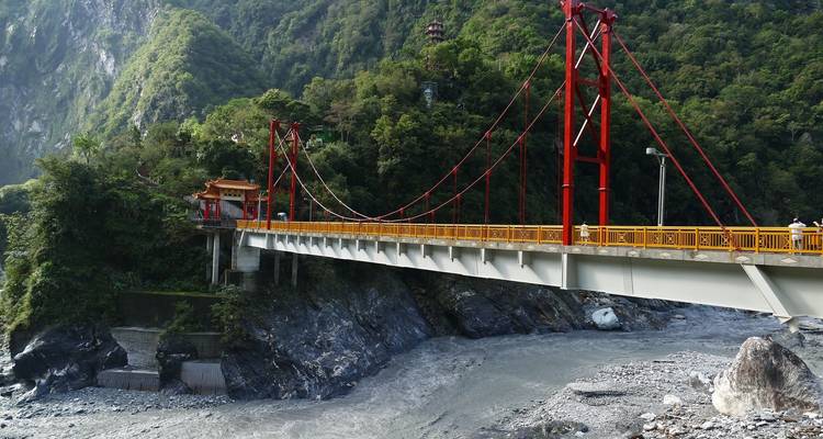 Pont rouge au-dessus d'une rivière rocheuse entourée de forêt.