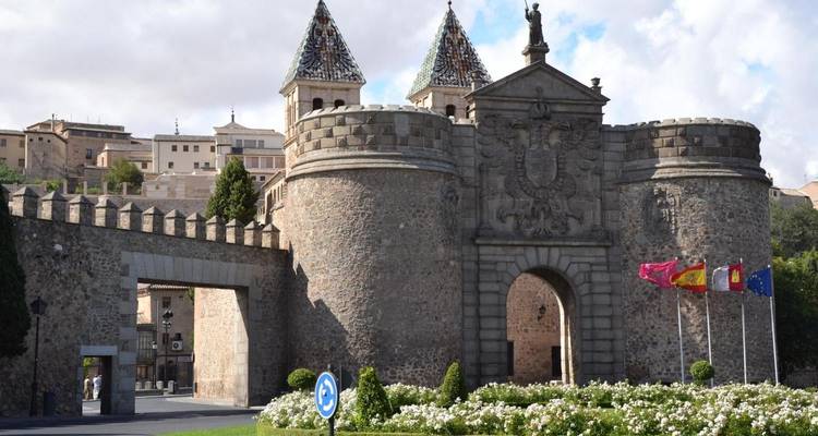 Une porte historique en pierre avec des drapeaux et des tours décoratives, probablement dans un environnement fortifié.