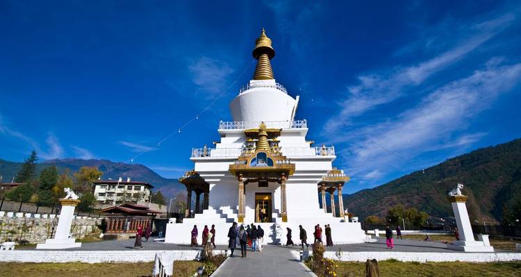 Weiße Stupa mit goldenen Akzenten und einer Gruppe von Menschen davor.
