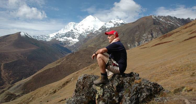 Person sitzt auf einem felsigen Hügel mit schneebedeckten Bergen in der Ferne.