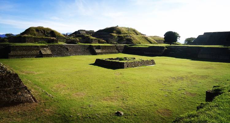 Sunlit grassy plaza surrounded by stepped stone platforms at Monte Albán archaeological site