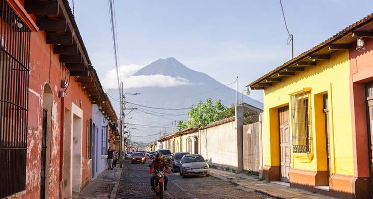 Cobbled street lined with colourful colonial houses leads to a mist-capped volcano in Antigua.
