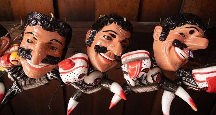 Row of brightly painted folk masks with exaggerated moustaches hanging on display.