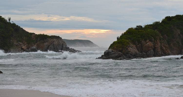 Rugged rocky coastline with crashing Pacific waves under a pastel evening sky