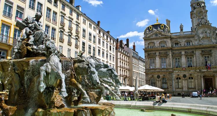 Fuente con estatua en una plaza de la ciudad rodeada de arquitectura clásica europea.