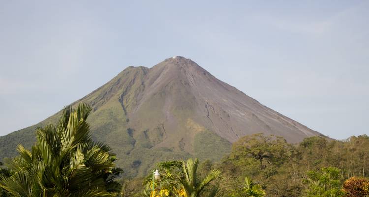 Cone-shaped Arenal Volcano towering above lush tropical foliage on a clear day