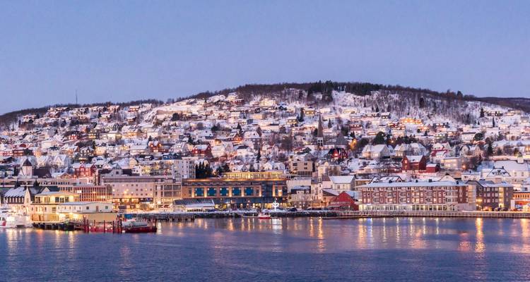 Vista del crepúsculo invernal de las casas nevadas de Tromsø y sus luces reflejadas en el puerto.