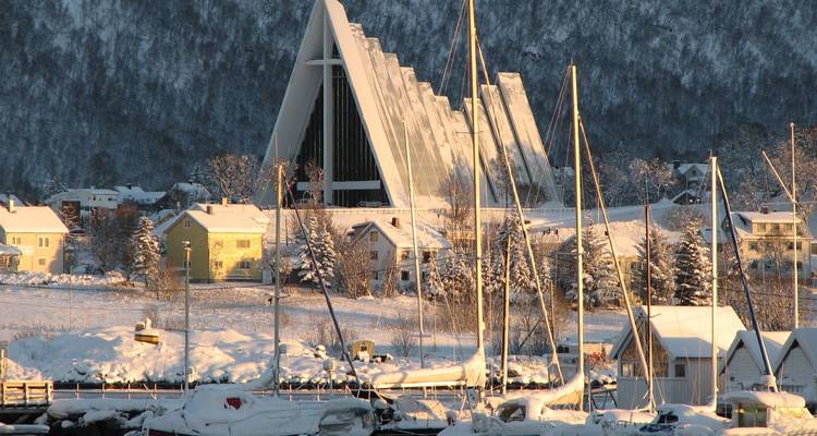 Vista enmarcada por la nieve de la Catedral Ártica con veleros y casas de invierno a lo largo del puerto.