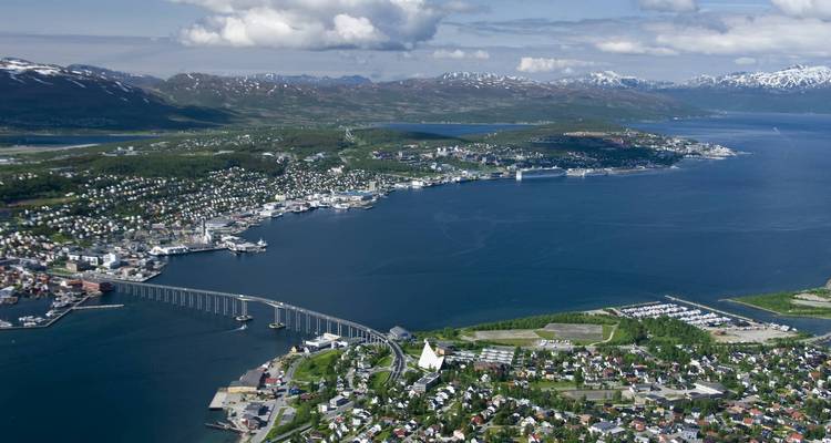 Luftpanorama der Insel Tromsø mit ihrer ikonischen Brücke und den umliegenden schneebedeckten Bergen, die einen blauen Fjord umgeben.