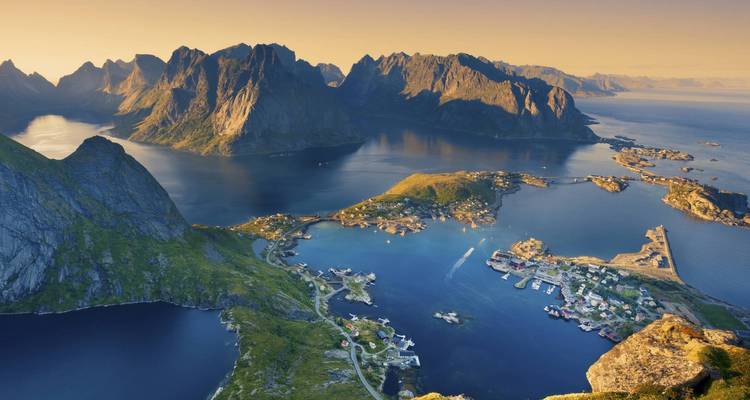 Atemberaubendes Luftbild zur goldenen Stunde des Dorfes Reine, eingebettet zwischen dramatischen Granitgipfeln und tiefblauen Wasserstraßen in Norwegens Lofoten-Inseln.