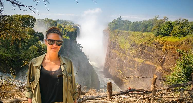 Une femme debout près d'une clôture en bois avec vue sur les chutes Victoria.