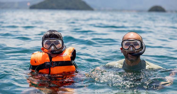 Un adulte et un enfant portant des gilets de sauvetage et des masques de plongée en apnée flottant dans une mer tropicale.