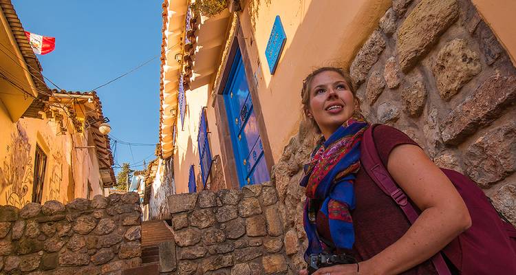 Voyageur souriant avec sac a dos se tenant dans une ruelle pavée étroite de maisons colorées de Cusco sous un ciel bleu éclatant.
