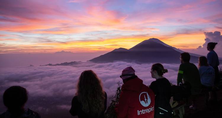 Des randonneurs observent un lever de soleil à couper le souffle au-dessus d'une mer de nuages avec des pics volcaniques se découpant en silhouette contre un ciel aux couleurs vives de rose et d'orange.
