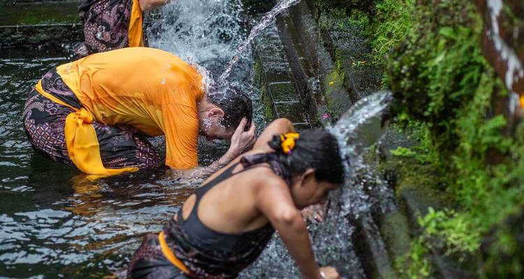 Les participants s'agenouillent sous des gargouilles en pierre effectuant un rituel traditionnel de purification par l'eau dans un bassin de temple.