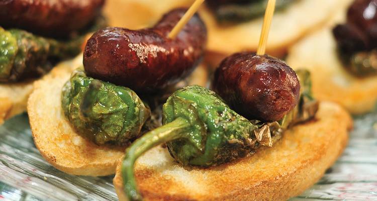 Amuse-gueule avec chorizo et poivrons verts sur une tranche de pain.