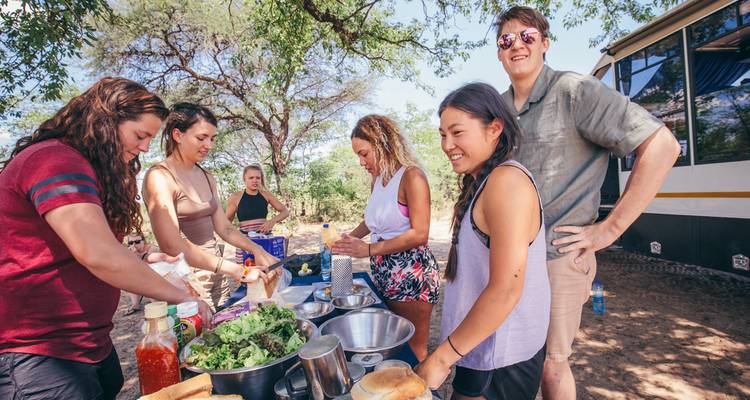 Personnes préparant de la nourriture en plein air à côté d'un bus touristique.