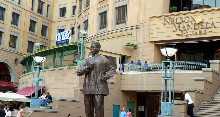 Standbeeld van Nelson Mandela op Mandela Square omringd door mensen.
