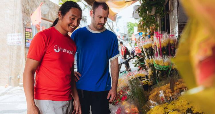 Deux voyageurs masculins consultent les offres de fleurs colorées à un étal de rue animé vietnamien.