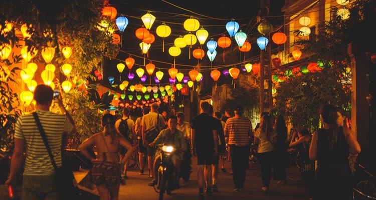 Una animada calle del mercado nocturno en Hoi An brilla con incontables faroles coloridos mientras multitudes pasean bajo las luces.