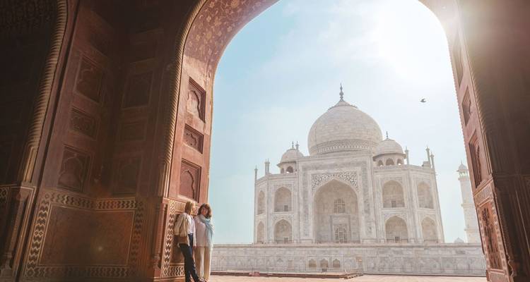 The Taj Mahal framed by an arch with two people standing in the foreground.