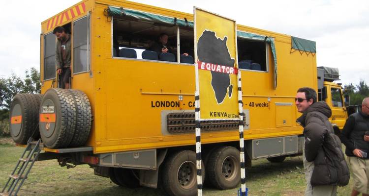 Groupe de touristes près d'un grand véhicule jaune de voyage overland avec le panneau de l'Équateur.