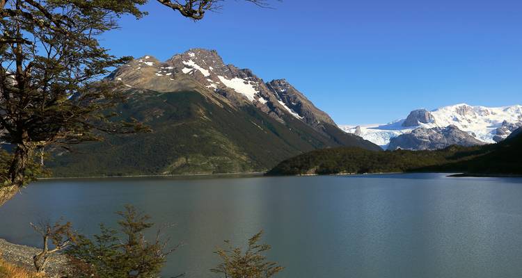 Serene lake surrounded by forested slopes and snow-tipped mountains with glacier.