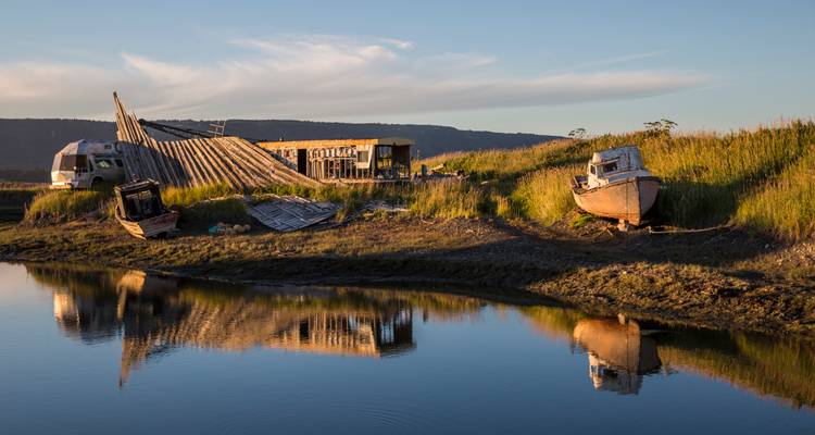 Abandoned wooden boats and collapsing shack reflect in calm water at sunset light
