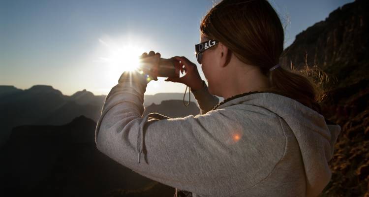 Personne prenant une photo, sur fond de montagnes ensoleillées.