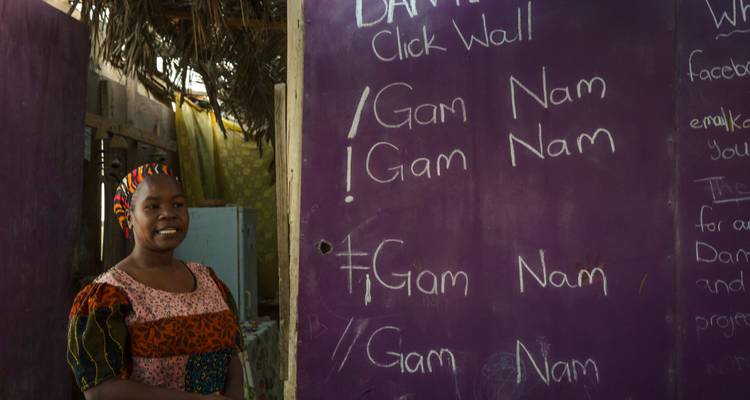 Smiling woman poses beside purple classroom wall showing click language examples.