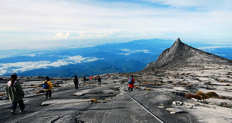 Les randonneurs descendent le plateau sommital en granit balayé par les vents du mont Kinabalu au-dessus d'une mer de nuages.
