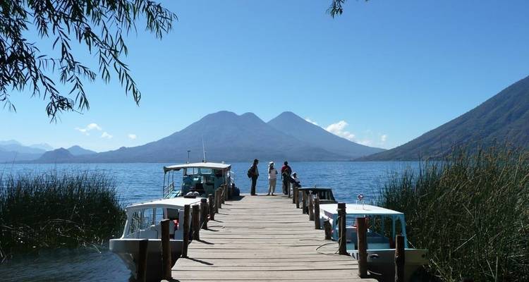 Lago rodeado de montañas, con barcas atracadas en un muelle de madera.