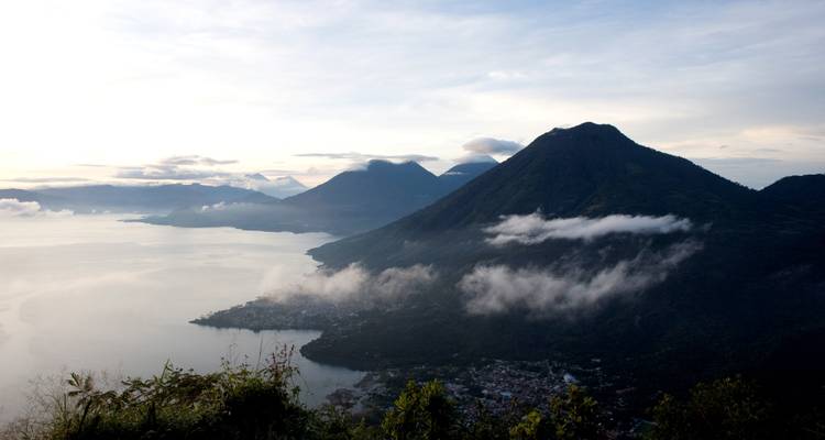 Vista de la ciudad junto al lago con nubes sobre las montañas.