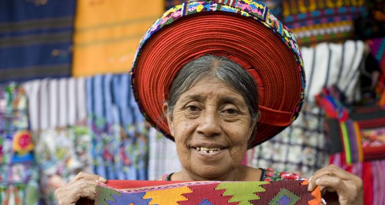 Anciana sonriente sosteniendo telas de colores, vestida con un traje tradicional.
