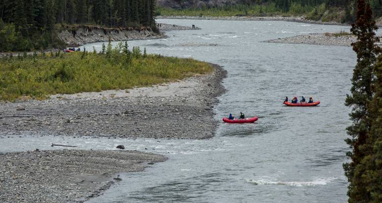 Plusieurs radeaux pneumatiques avec des passagers descendent une large rivière rocheuse