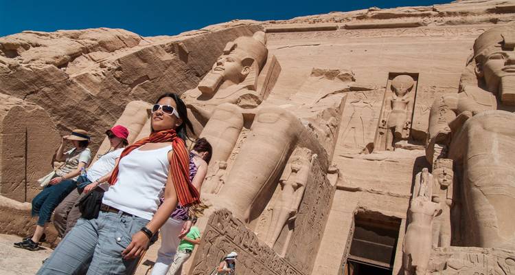 Los visitantes exploran las estatuas colosales y la fachada tallada de Abu Simbel bajo cielos azules y brillantes.